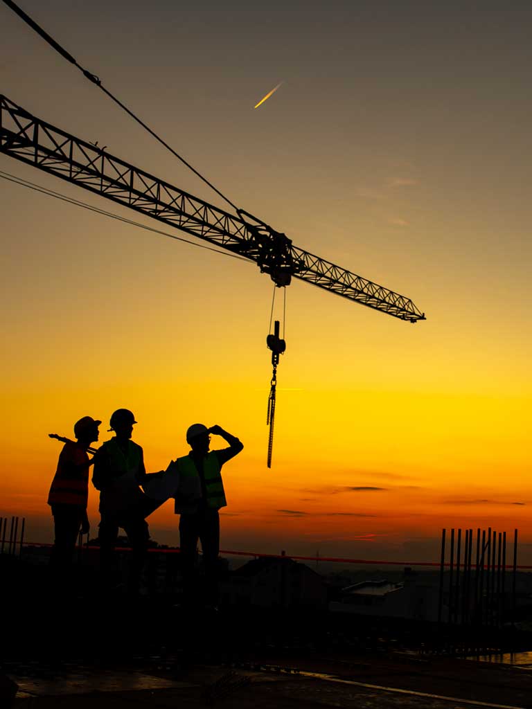 Workers surveying construction site at sunset with crane in the background.